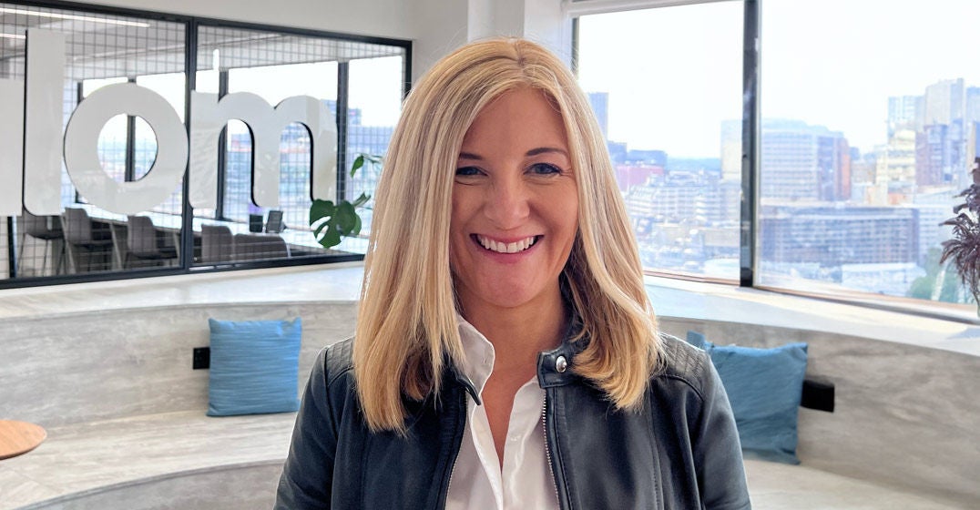 Headshot of Manchester's general manager, Caroline Grant, wearing a black jacket and white shirt, standing in front of the windows at the local Slalom office.