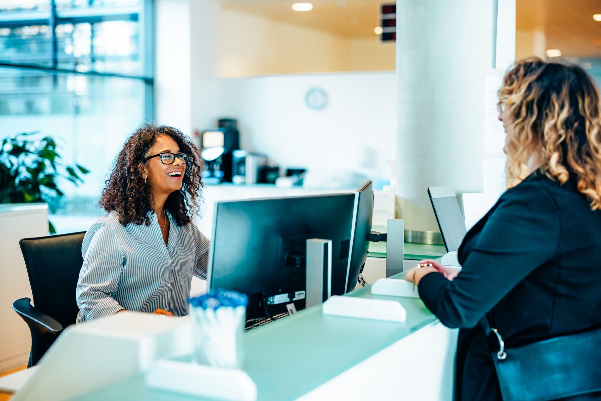 Receptionist assisting a woman standing at front desk. Woman standing at the reception talking with a friendly receptionist behind the desk of municipality office.