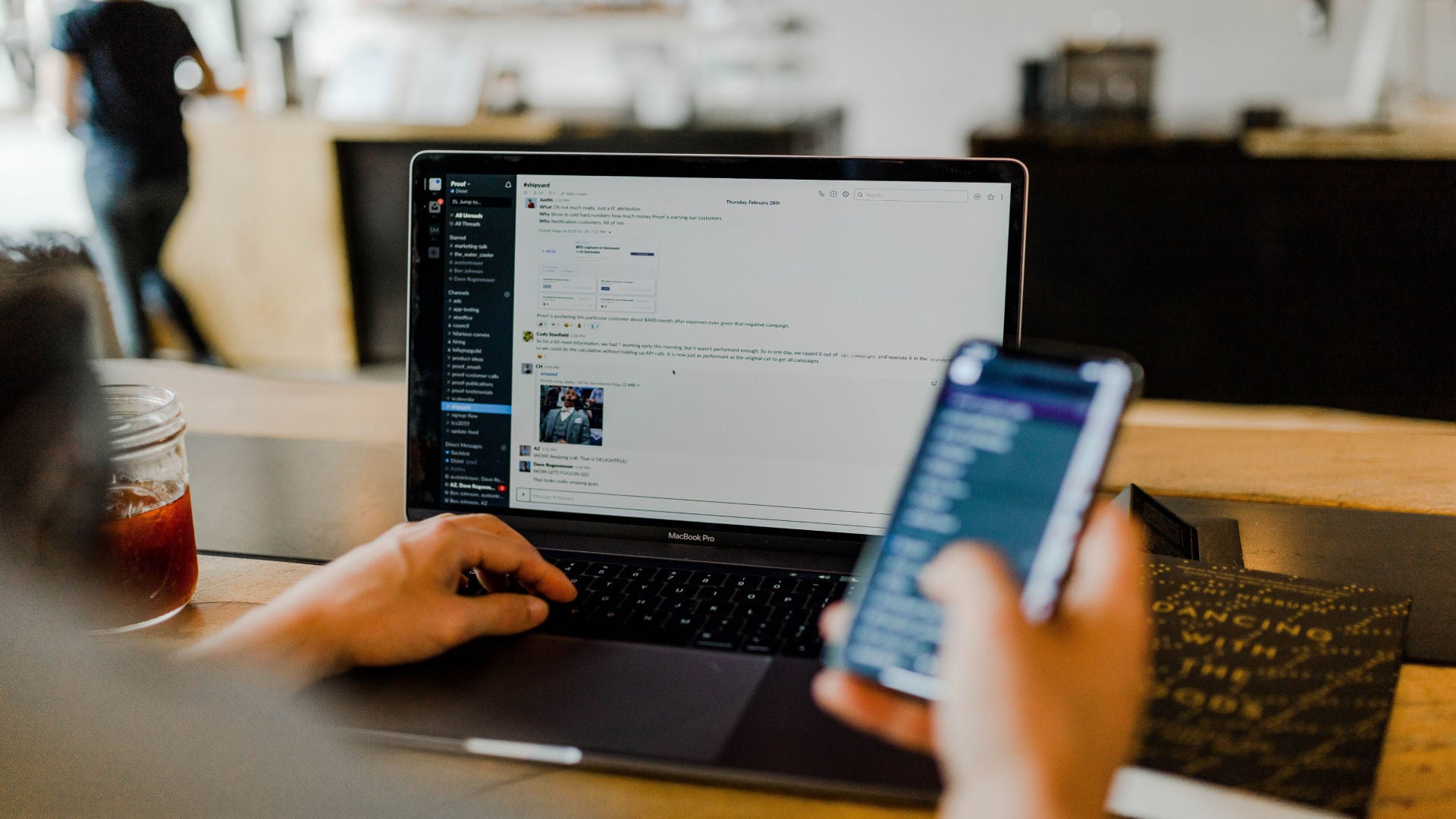 Person using a laptop and holding a phone.