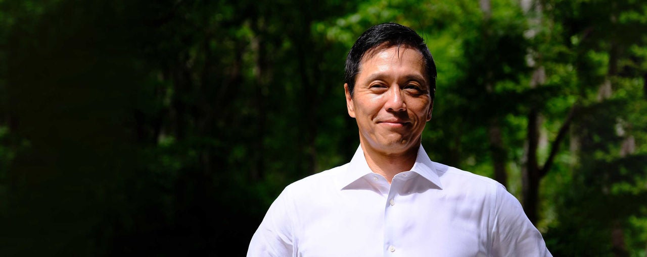 Headshot of Japan's general manager, Ko Asami, wearing a white shirt against a forested backdrop.