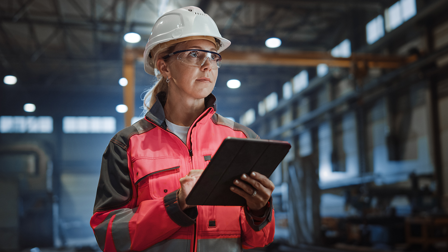 Professional Heavy Industry Engineer/Worker Wearing Safety Uniform and Hard Hat Uses Tablet Computer. Serious Successful Female Industrial Specialist Walking in a Metal Manufacture Warehouse.