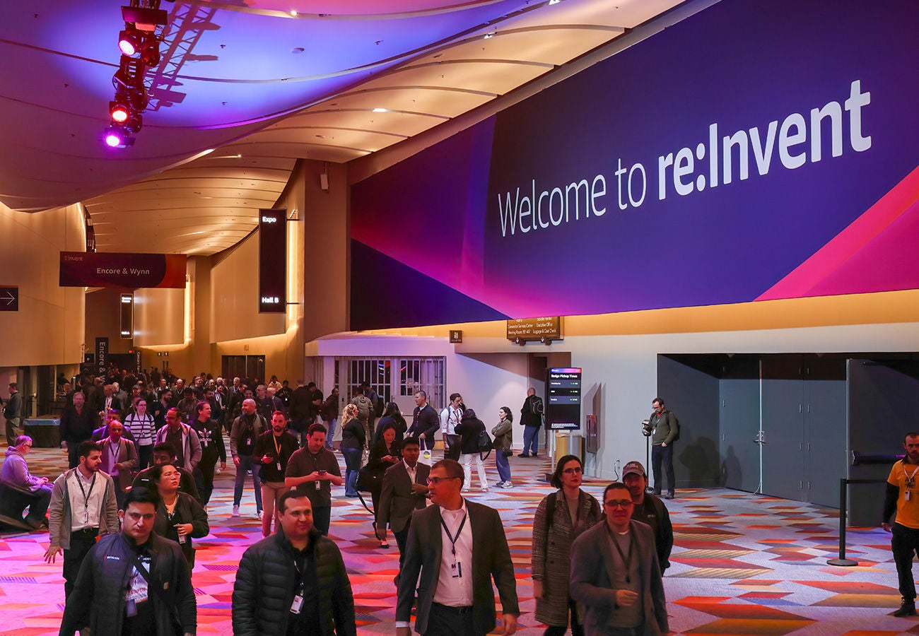 Crowd of people walking by a set of doors above which a banner reads: “Welcome to re:Invent