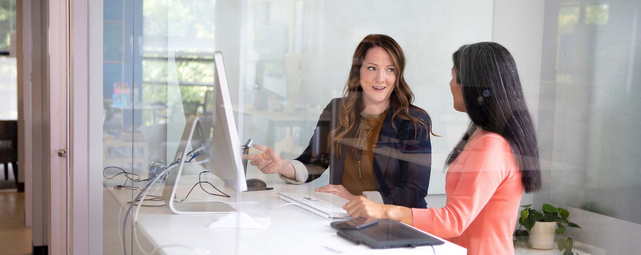 Two female workers in office collaborating on a computer.