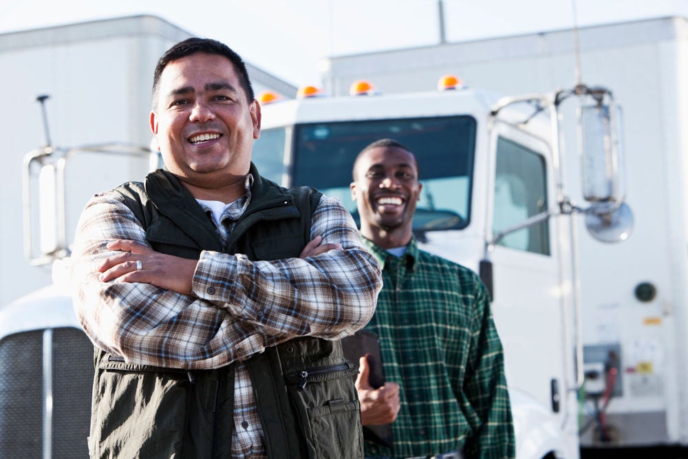 Two truck drivers in front of their truck.