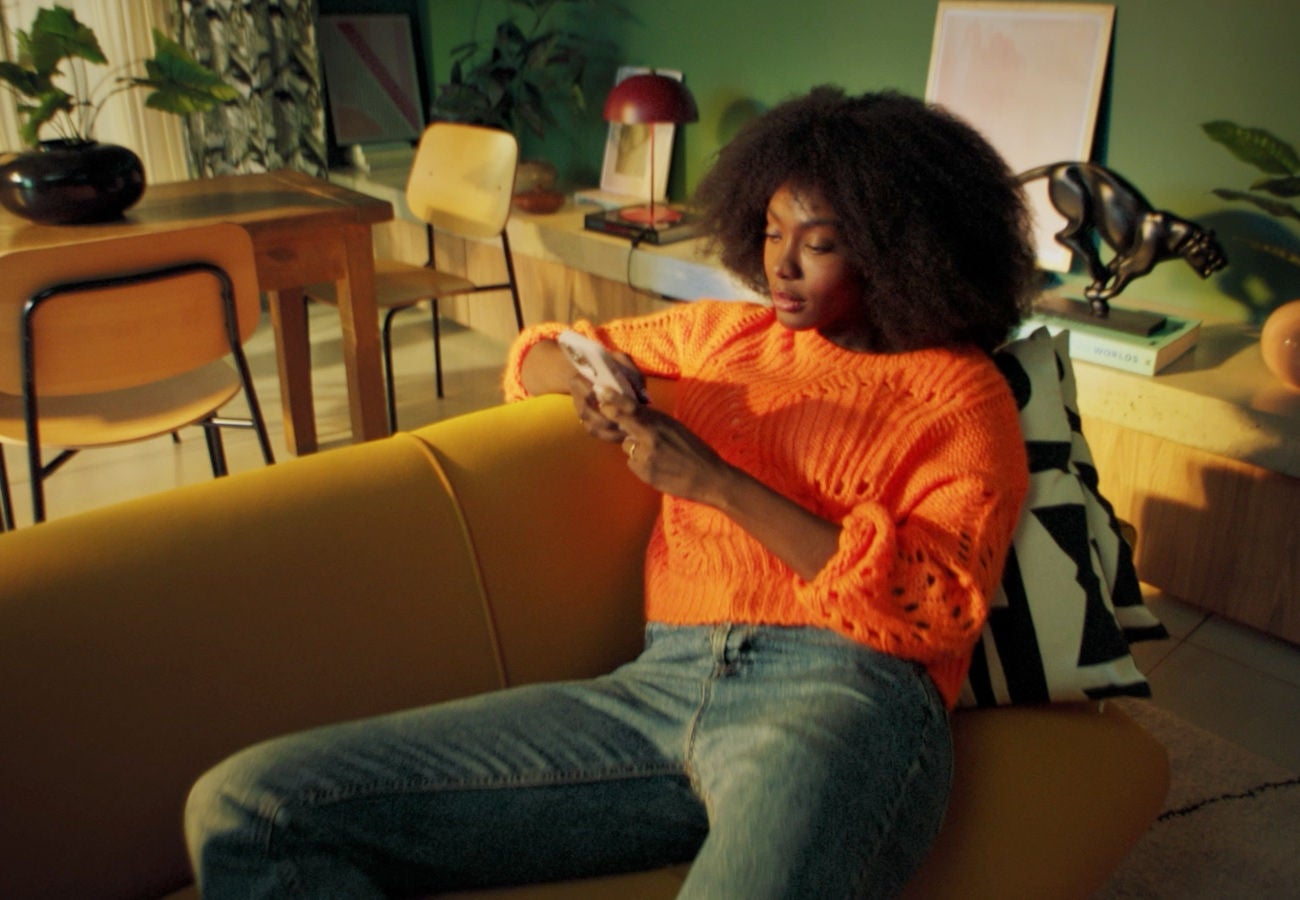 Woman looking at a mobile device while seated on a couch in a living room of a home.