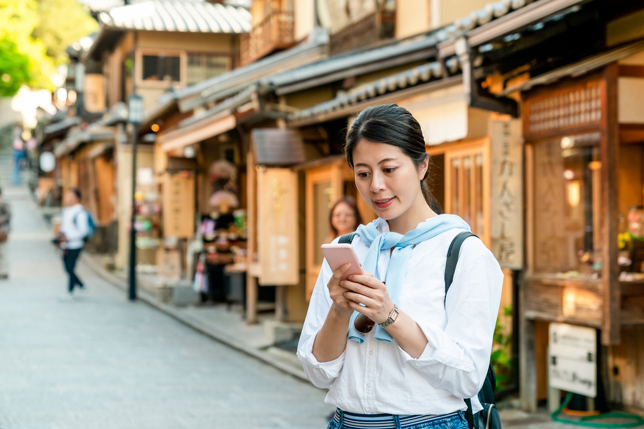 cheerful asian Japanese female visitor reading online travel info on cellphone on the traditional shopping street at Ninenzaka and Sannenzaka in Kyoto japan