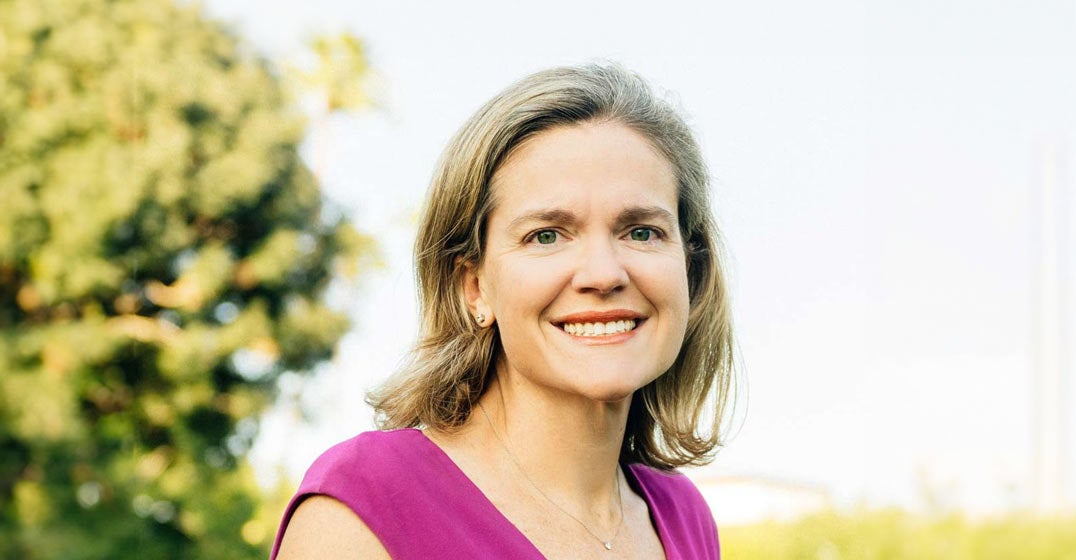 Phoenix general manager Sarah Moesker in a fuchsia dress, standing on a grassy field with a tree in the background..