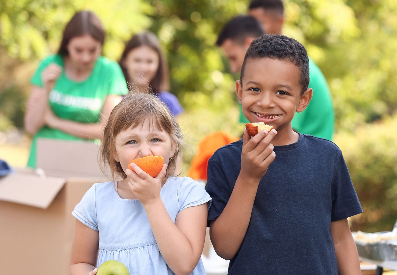 Two children enjoy fruit outside ona. sunny day in the park.