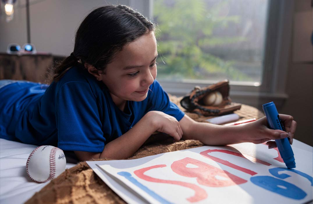 Jeune partisane de baseball confectionnant une affiche pour le prochain match de baseball.