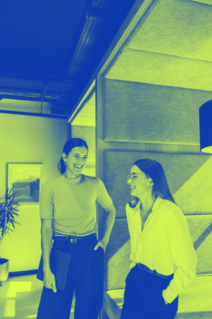 Successful businesswomen sharing a laugh in the office. Two young female entrepreneurs laughing cheerfully while standing together in a modern workspace.