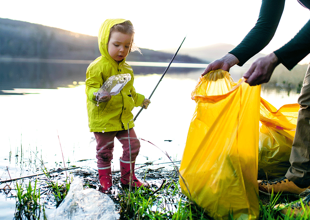 Father with small daughter collecting rubbish outdoors in nature, plogging concept.